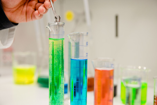 A row of test tubes with different colored liquids, a hand is filling something with